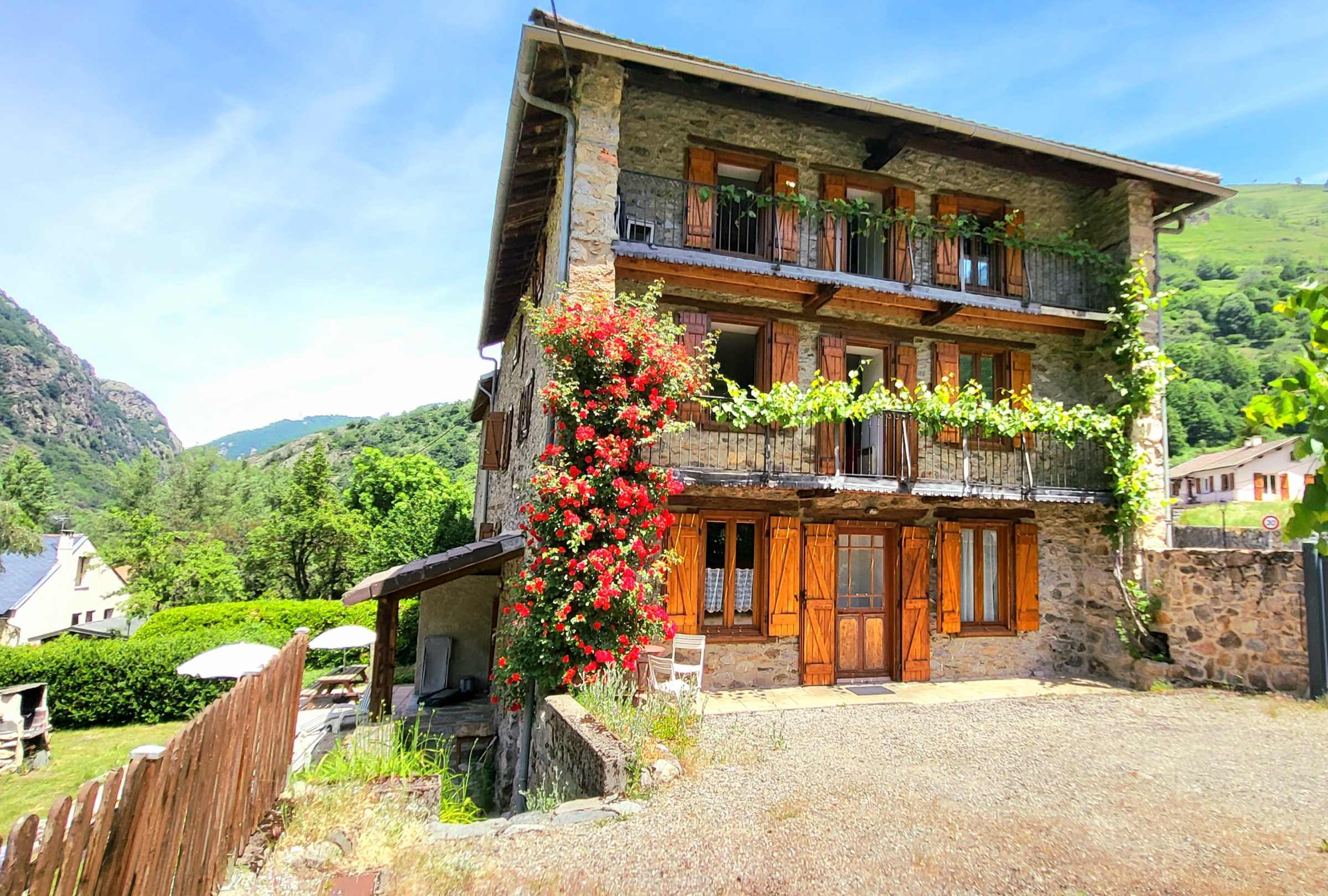 La maison en pierre, sa façade fleurie et ses balcons, au pied des montagnes